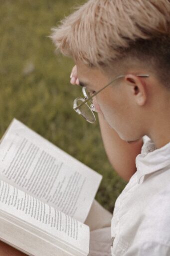 young man in glasses reading book in park reader