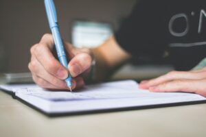 person holding writing time blue ballpoint pen writing in notebook